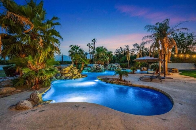 pool at dusk featuring a patio and pool water feature