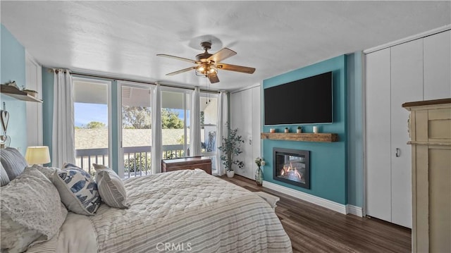 bedroom with a glass covered fireplace, two closets, baseboards, dark wood-style floors, and a ceiling fan