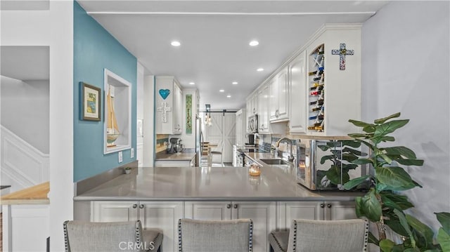 kitchen featuring sink, a kitchen breakfast bar, white cabinets, a barn door, and kitchen peninsula