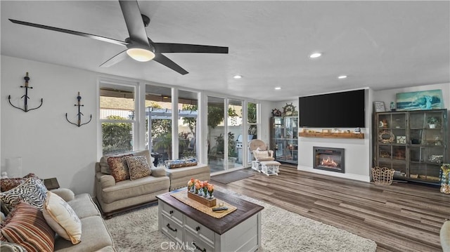 living room featuring a glass covered fireplace, a ceiling fan, recessed lighting, and wood finished floors