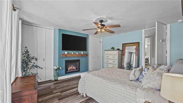 bedroom with ceiling fan, wood finished floors, and a lit fireplace