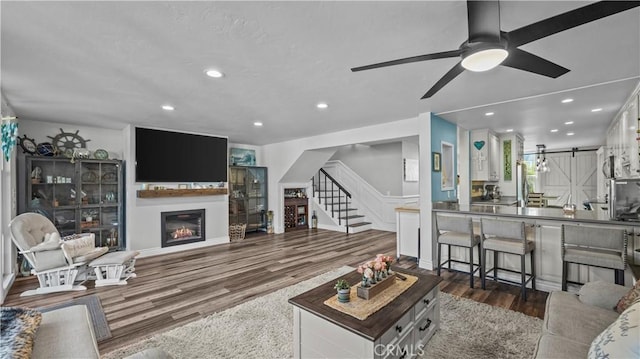 living room with ceiling fan, a barn door, stairs, recessed lighting, and wood finished floors
