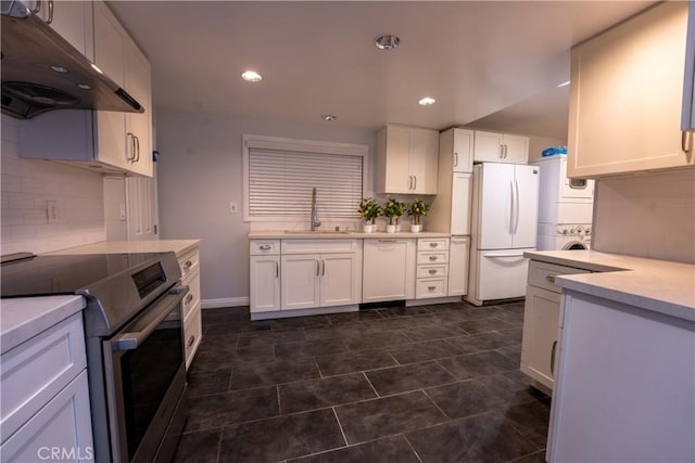 kitchen with white cabinetry, sink, stainless steel range with electric stovetop, stacked washer and clothes dryer, and white fridge