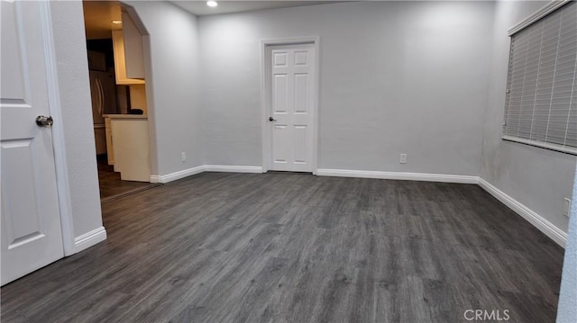 empty room with arched walkways, dark wood-type flooring, and baseboards