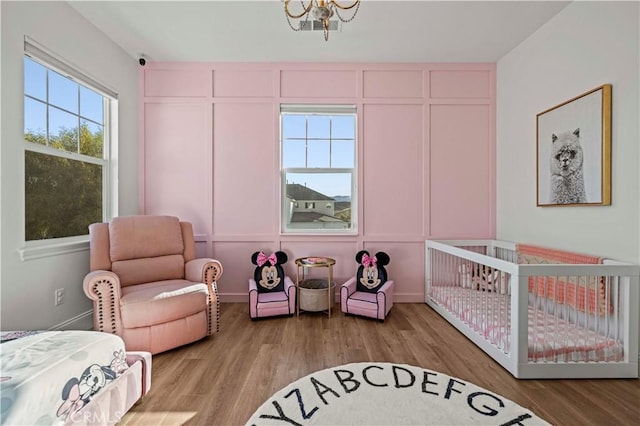 bedroom featuring a crib, a notable chandelier, and light hardwood / wood-style flooring