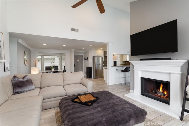 living room featuring ceiling fan, ornamental molding, decorative columns, and light wood-type flooring