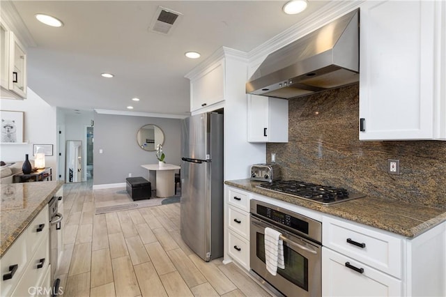 kitchen with white cabinetry, dark stone countertops, wall chimney exhaust hood, and appliances with stainless steel finishes