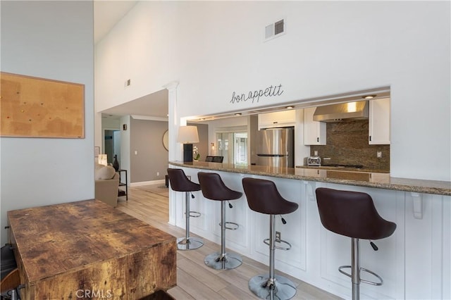 kitchen featuring a kitchen breakfast bar, stainless steel fridge, kitchen peninsula, stone counters, and range hood