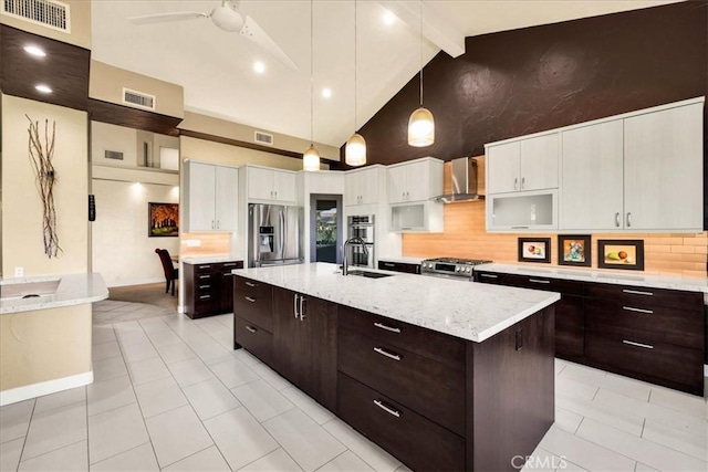 kitchen featuring wall chimney exhaust hood, sink, hanging light fixtures, stainless steel appliances, and a kitchen island with sink