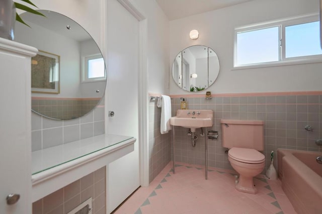 bathroom with tile walls, a washtub, toilet, and a healthy amount of sunlight