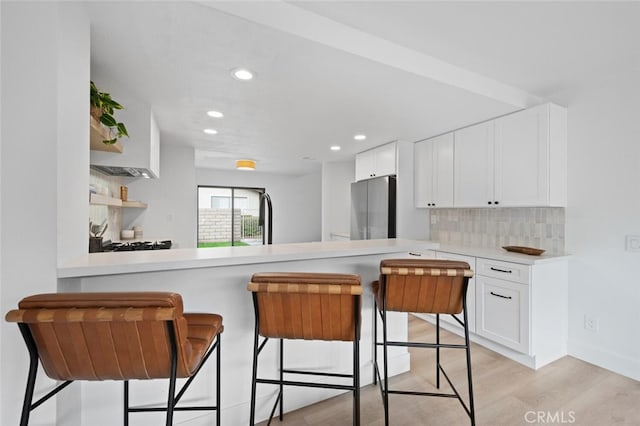 kitchen with a kitchen bar, white cabinetry, stainless steel refrigerator, kitchen peninsula, and backsplash