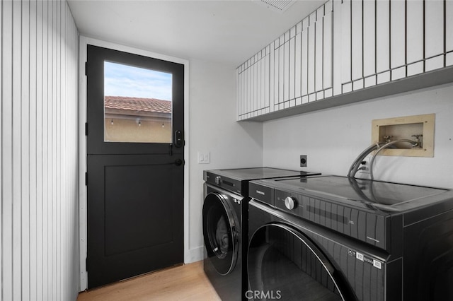 clothes washing area featuring washer and clothes dryer, cabinets, and light wood-type flooring