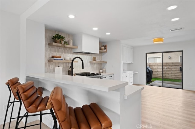 kitchen featuring a breakfast bar area, tasteful backsplash, white cabinets, kitchen peninsula, and light wood-type flooring