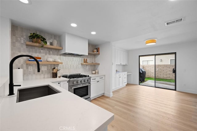 kitchen with sink, light wood-type flooring, white cabinets, high end stainless steel range oven, and backsplash