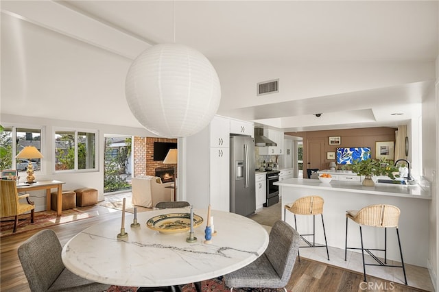 dining area with high vaulted ceiling, visible vents, light wood-style floors, and a brick fireplace