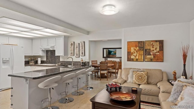 kitchen featuring sink, a breakfast bar area, kitchen peninsula, white fridge with ice dispenser, and white cabinets