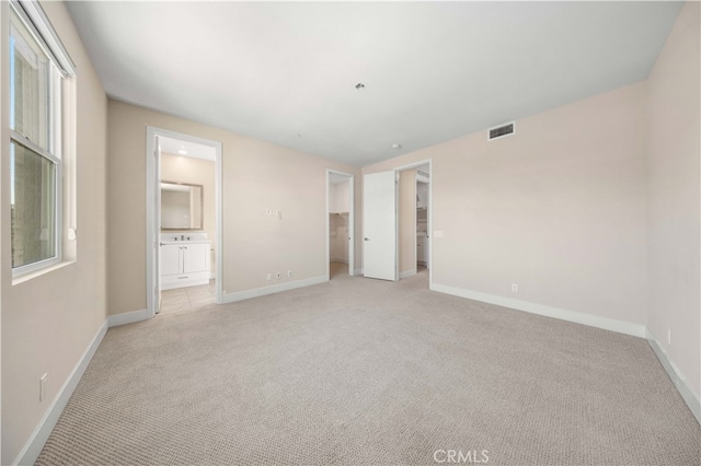 unfurnished bedroom with a spacious closet, light colored carpet, and ensuite bathroom