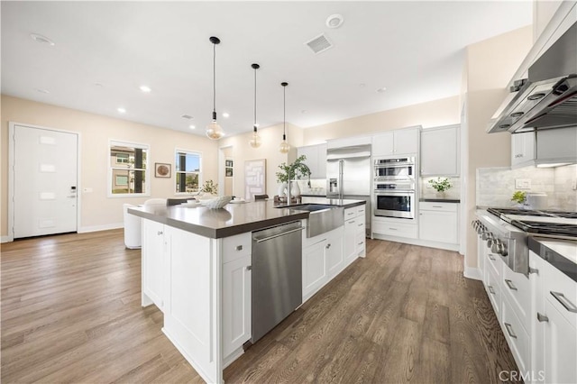 kitchen with extractor fan, a center island with sink, white cabinets, and appliances with stainless steel finishes