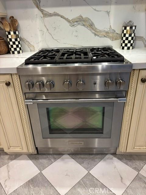 room details with cream cabinetry, high end range, and decorative backsplash