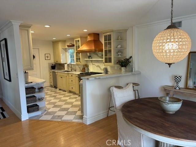 kitchen with premium range hood, sink, hanging light fixtures, stainless steel dishwasher, and cream cabinets