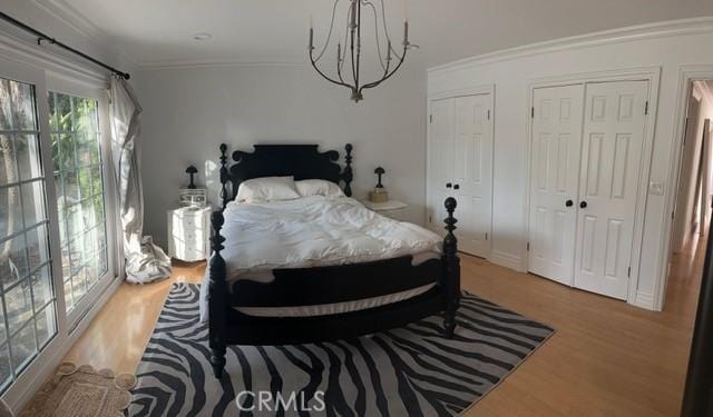 bedroom featuring multiple closets, ornamental molding, an inviting chandelier, and light hardwood / wood-style flooring