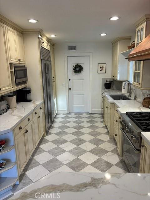 kitchen featuring high end appliances, sink, light stone counters, and cream cabinets