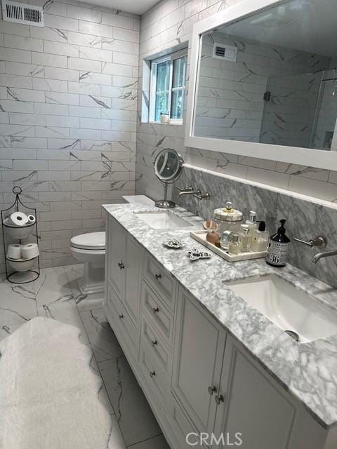 bathroom featuring a shower with shower door, tile walls, decorative backsplash, vanity, and toilet