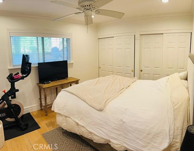 bedroom with multiple closets, ceiling fan, ornamental molding, and light hardwood / wood-style flooring