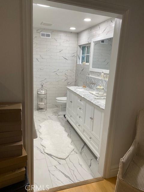 bathroom featuring vanity, toilet, and tile walls