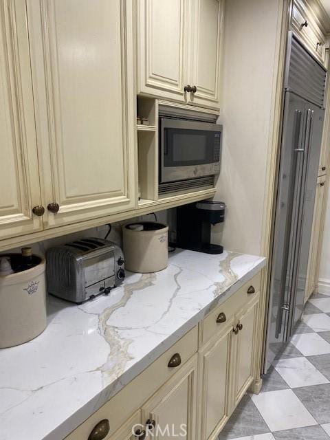 kitchen featuring built in appliances, light stone counters, and cream cabinetry