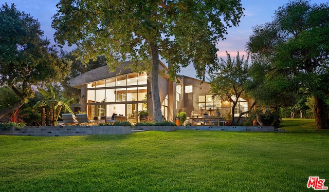 back house at dusk with a lawn