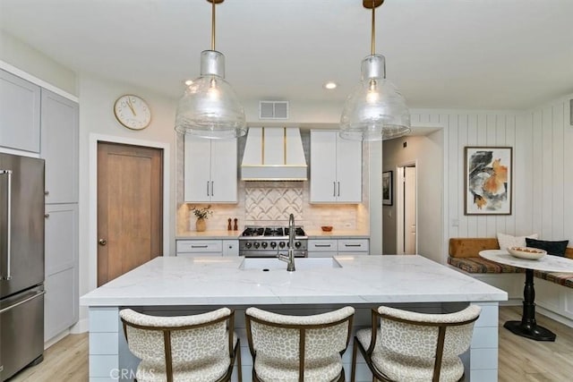 kitchen with high end appliances, hanging light fixtures, a kitchen island with sink, and custom range hood