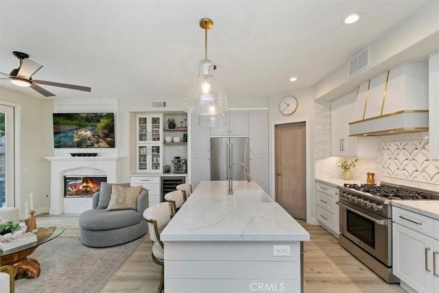 kitchen featuring sink, an island with sink, pendant lighting, stainless steel appliances, and white cabinets