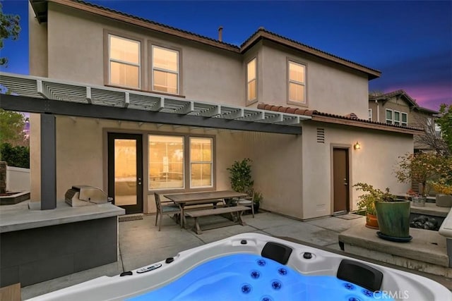 back house at dusk featuring an outdoor hot tub, a pergola, and a patio