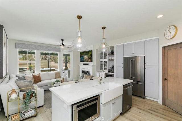 kitchen with stainless steel appliances, sink, a center island with sink, and light wood-type flooring