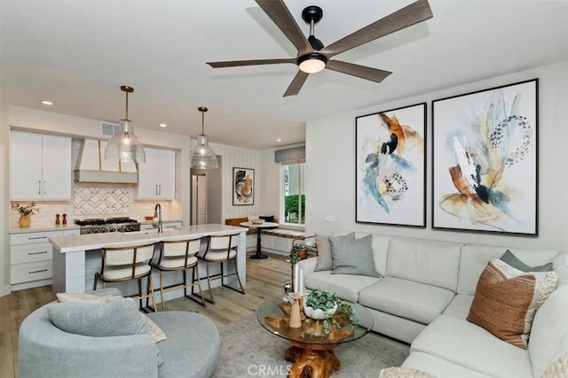 living room with sink, ceiling fan, and light wood-type flooring