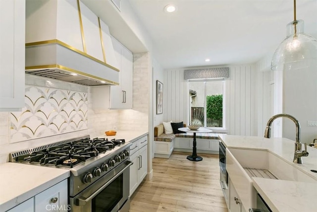 kitchen with white cabinetry, decorative light fixtures, stainless steel range with gas cooktop, and premium range hood