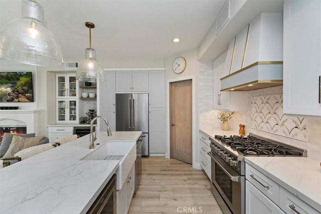 kitchen featuring sink, premium appliances, custom range hood, pendant lighting, and white cabinets