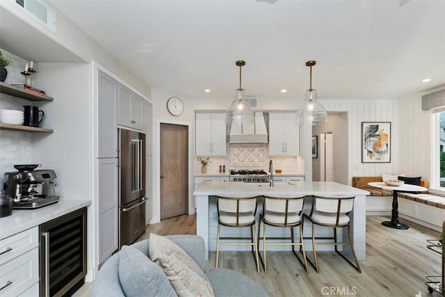 kitchen featuring decorative light fixtures, an island with sink, high end refrigerator, wine cooler, and stove