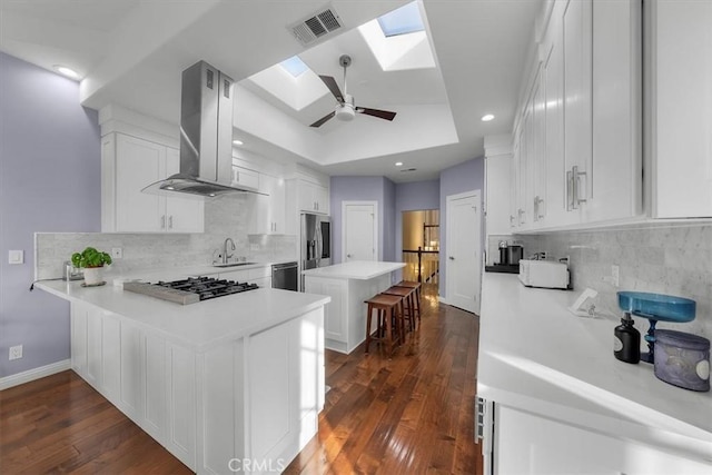 kitchen with island range hood, a skylight, white cabinetry, a kitchen bar, and a tray ceiling