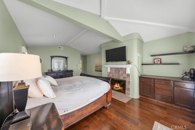 bedroom featuring lofted ceiling with beams, a tiled fireplace, and dark wood-type flooring