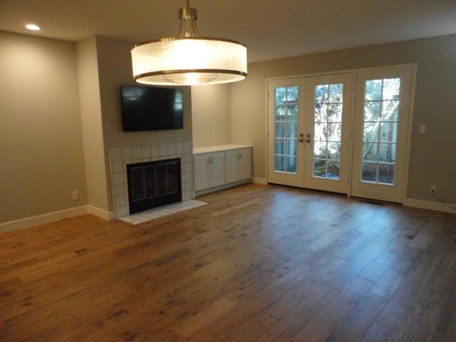 unfurnished living room with french doors, wood-type flooring, and a tile fireplace