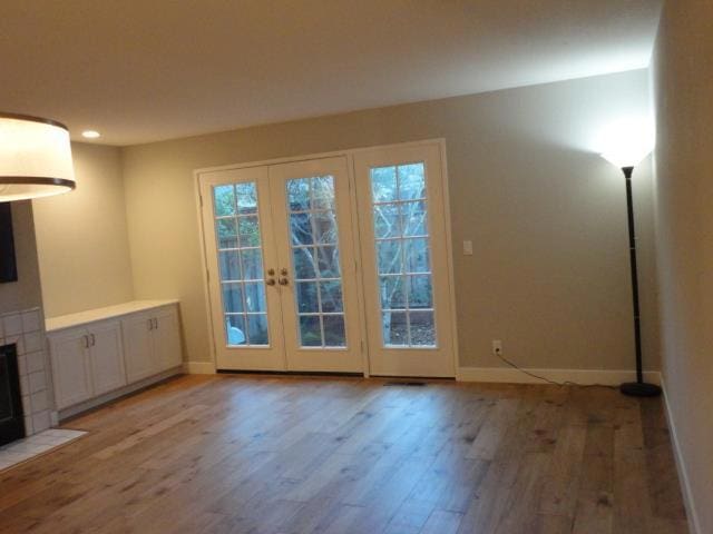 doorway to outside with french doors, a tile fireplace, and light wood-type flooring