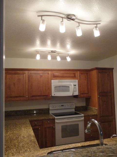 kitchen featuring sink, white appliances, a textured ceiling, and stone counters