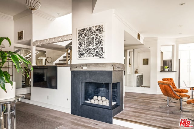 living room with a multi sided fireplace, ornamental molding, and hardwood / wood-style floors