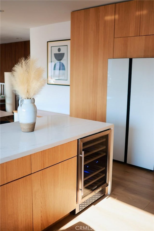 kitchen featuring light stone countertops, light hardwood / wood-style floors, beverage cooler, and refrigerator