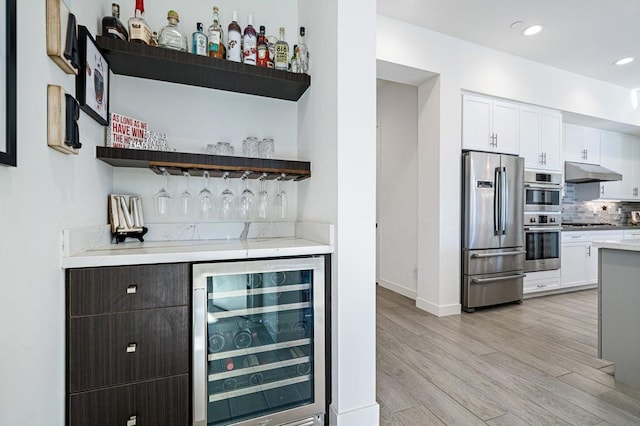 bar featuring white cabinetry, light wood-type flooring, stainless steel appliances, beverage cooler, and backsplash