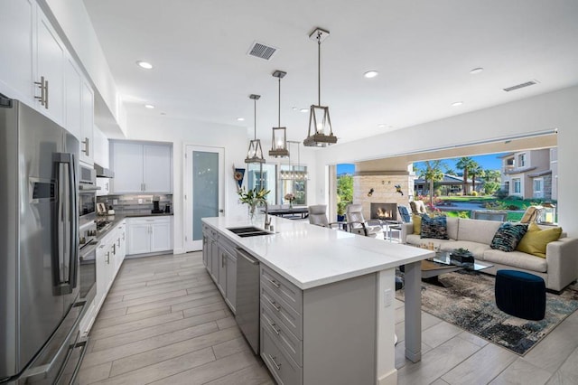 kitchen with sink, white cabinetry, stainless steel appliances, a center island with sink, and decorative light fixtures