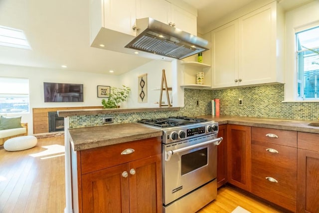 kitchen featuring backsplash, island range hood, stainless steel gas range oven, white cabinets, and kitchen peninsula