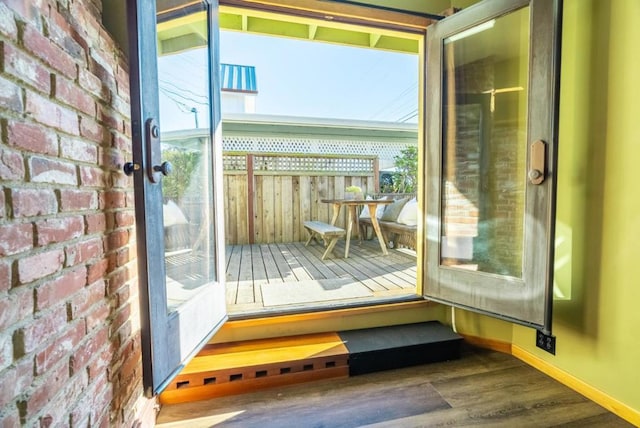 doorway to outside with dark wood-type flooring and brick wall